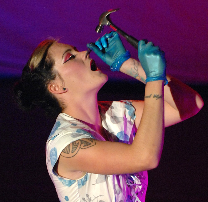 Magenta Diamond gently hammers a nail into her nose. 